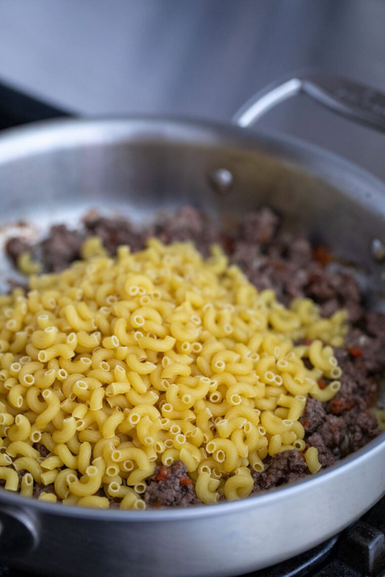 Adding dry macaroni to skillet.